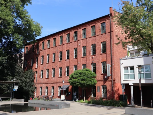 Stadtbibliothek-Erich-Gutenberg-Haus (2).JPG Backsteingebäude mit vielen Fenstern, Bäumen umgeben; modernes Design, Platz mit Wasserbecken vorne.