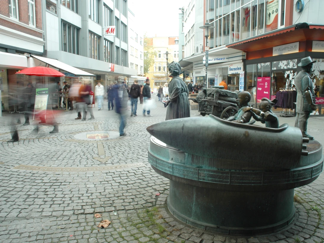 DSC_0698.JPG Passanten flanieren an einer Brunnen-Skulptur auf einer belebten Einkaufsstraße entlang.
