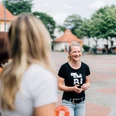 Kiez-Tour Bielefeld.jpg Lächelnde Frau in schwarzem T-Shirt steht in einer kleinen Gruppe auf einem gepflasterten Platz.