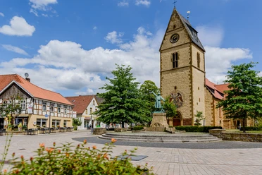 Kirchplatz Gemeinde Steinhagen (C) pro Wirtschaft GT, Mario Wallenfang.jpeg Uhrturm und Fachwerkhäuser an einem sonnigen Tag auf einem idyllischen Marktplatz.