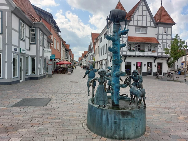 Bronzene Figuren eines Mädchens und Ziegen beim Kanzlerbrunnen in einer gepflasterten Fußgängerzone.