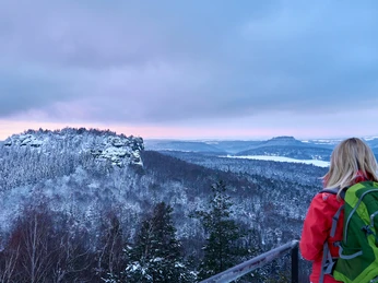 Aussicht vom Papststein Eine Person mit rotem Rucksack blickt von einem Aussichtspunkt auf eine verschneite Berglandschaft.A person with a red rucksack looks out over a snow-covered mountain landscape from a vantage point.Osoba s červeným batohem se dívá z vyhlídky na zasněženou horskou krajinu.Osoba z czerwonym plecakiem spogląda z punktu widokowego na ośnieżony górski krajobraz.Een persoon met een rode rugzak kijkt uit over een besneeuwd berglandschap vanaf een uitkijkpunt.Una persona con uno zaino rosso osserva un paesaggio montano innevato da un punto panoramico.