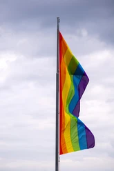 Cologne Pride Eine bunte Regenbogenflagge weht im Wind vor bewölktem Himmel.