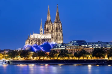 Cologne Cathedral Evening sky above the majestic Cologne Cathedral, illuminated, surrounded by modern buildings and the glittering Rhine promenade.