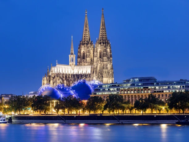 Cologne Cathedral Evening sky above the majestic Cologne Cathedral, illuminated, surrounded by modern buildings and the glittering Rhine promenade.