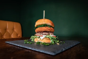 Bulldog Ein künstlerisch angerichteter Burger mit mehreren Schichten, serviert auf einem dunklen Schieferbrett.