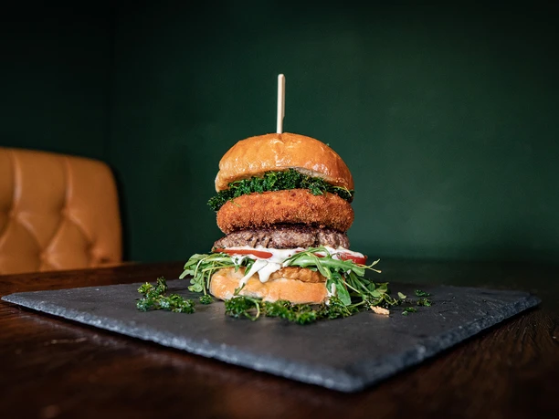 Bulldog Ein künstlerisch angerichteter Burger mit mehreren Schichten, serviert auf einem dunklen Schieferbrett.