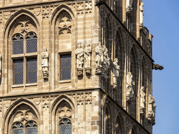 Historic town hall The façade of Cologne's historic town hall features detailed figures and Gothic architecture. The sun's rays highlight the fine stone carvings on the sand-colored towers.