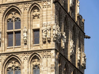 Historisches Rathaus Die Fassade des Historischen Rathauses Köln zeigt detailreiche Figuren und gotische Architektur. Sonnenstrahlen heben die feinen Steinmetzarbeiten auf den sandfarbenen Türmen hervor. The façade of Cologne's historic town hall features detailed figures and Gothic architecture. The sun's rays highlight the fine stone carvings on the sand-colored towers.
