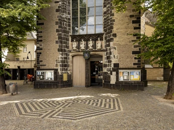Saint Severin Kirchenportal von Sankt Severin in Köln, eingerahmt von Bäumen auf einem gepflasterten Platz.Church portal of St. Severin in Cologne, framed by trees on a paved square.