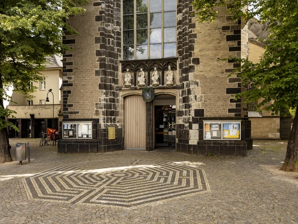 Saint Severin Church portal of St. Severin in Cologne, framed by trees on a paved square.