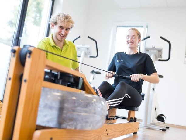 221021-FotoChristianSchwier-0933.jpg Ein junger Mann und eine Frau trainieren lachend an einem Holz-Wasserrudergerät in einem Fitnessstudio.