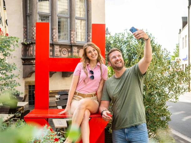 Couple takes selfie on red chair in front of historic town hall