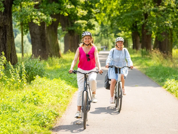 Hoexter-Landesgartenschaugelände Weserradweg-Stadt Hoexter-D. Ketz-2023-423.jpg Zwei Frauen genießen eine Radtour durch eine schöne, dicht bewachsene Eichenallee