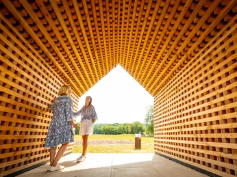 Zwei Frauen unterhalten sich in einem Holzkubus aus kreuzweise geschichteten Holzlatten
