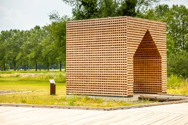 Holzkubus aus kreuzweise geschichteten Holzlatten im Archäologiepark