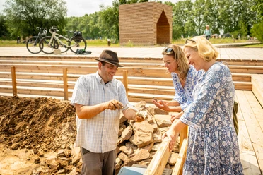 Archäologe präsentiert zwei Frauen einen gefundenen Tierknochen