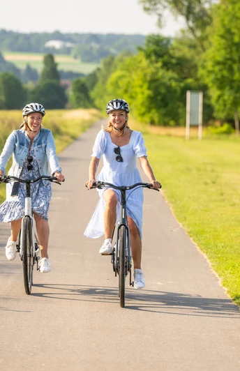 Hoexter-Freizeitanlage Godelheimer See-Stadt Hoexter-D. Ketz-2023-219.jpg Zwei Frauen radeln auf dem Weser-Radweg entlang eines Badesees
