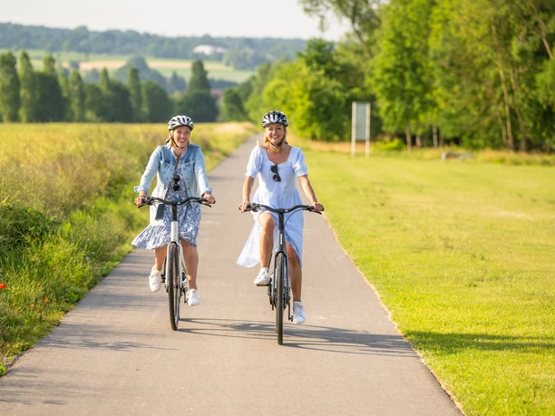 Hoexter-Freizeitanlage Godelheimer See-Stadt Hoexter-D. Ketz-2023-219.jpg Zwei Frauen radeln auf dem Weser-Radweg entlang eines Badesees