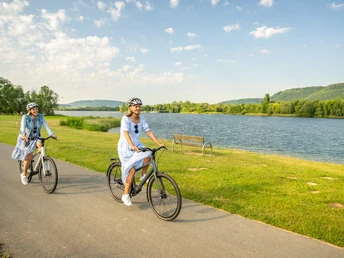 Hoexter-Freizeitanlage Godelheimer See-Stadt Hoexter-D. Ketz-2023-218.jpg Zwei Frauen radeln auf dem Weser-Radweg entlang eines Badesees