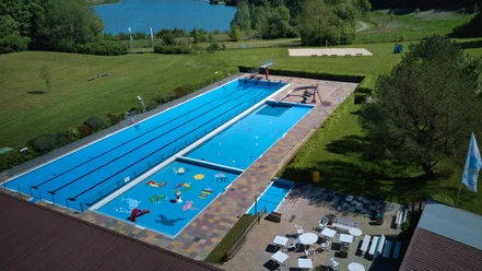 Großes Freibad mit Schwimm- und Planschbecken, umgeben von grüner Landschaft und Spielbereichen.