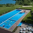 Großes Freibad mit Schwimm- und Planschbecken, umgeben von grüner Landschaft und Spielbereichen.