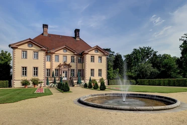 Schieder Schloss Das Schieder Schloss mit symmetrischem Park und zentralem Springbrunnen vor einem klaren, blauen Himmel.