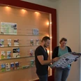 Zwei Personen betrachten in einem Informationszentrum Karten und Prospekte an einer beleuchteten Wand.