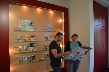 Tourist Info Zwei Personen betrachten in einem Informationszentrum Karten und Prospekte an einer beleuchteten Wand.