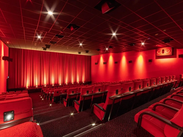 Een bioscoopzaal met rode stoelen, een rood gordijn en warme verlichting vlak voor het begin van een filmvertoning