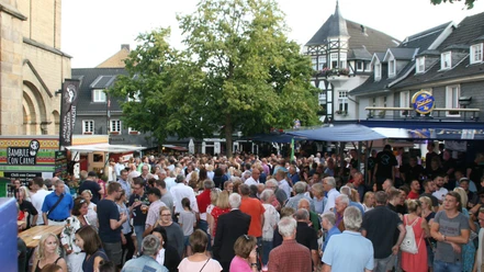Heimatfest Eine große Menschenmenge bei einem Heimatfest im Freien mit Ständen und alten Fachwerkhäusern im Hintergrund.