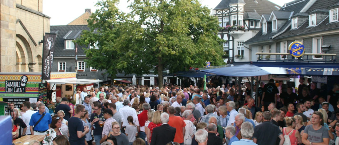 Heimatfest Eine große Menschenmenge bei einem Heimatfest im Freien mit Ständen und alten Fachwerkhäusern im Hintergrund.