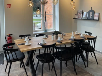 Gemütlicher Sitzbereich mit Holz- und Metalltisch, Hängelampen, acht schwarzen Stühlen und gedecktem Tisch.