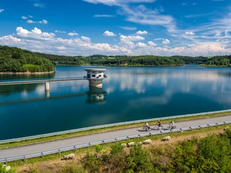 Große Dhünntalsperre Radsportler am Ufer der Talsperre Wermelskirchen, umgeben von grünen Hügeln und blauem Himmel.