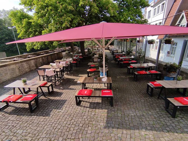 Sonnenterasse Ein sonniger Außenbereich mit roten Sonnenschirmen und Tischgruppen auf einem gepflasterten Hof.