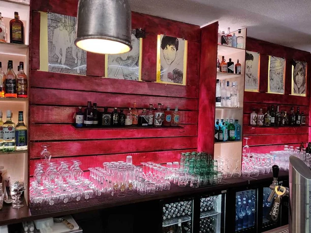 Bar Eine Bar mit beleuchteten Regalen voll Gläsern und Spirituosenflaschen vor einer roten Wand.