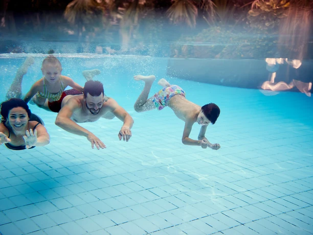 BS154915 Vier Menschen schwimmen fröhlich nebeneinander im klaren Wasser eines Schwimmbeckens.