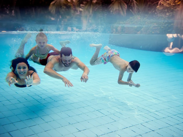 Center-parcs-bispinger-heide-familie-aqua-mundo.jpg Vier Menschen schwimmen fröhlich nebeneinander im klaren Wasser eines Schwimmbeckens.