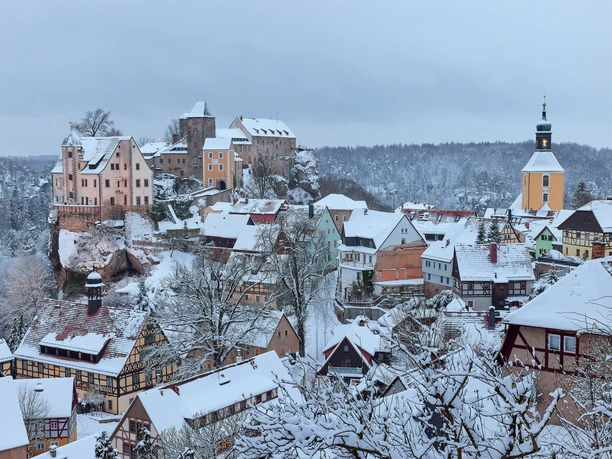 Ausblick auf Hohnstein im Winter Verschneite Altstadt mit Fachwerkhäusern und einer Burg auf einem Hügel; im Hintergrund ein Kirchturm, winterliche Atmosphäre.