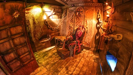 Escape Room Osnabrück.jpg Ein Piratenszenario in einem hölzernen Escape Room mit stimmungsvoller Beleuchtung und Requisiten.