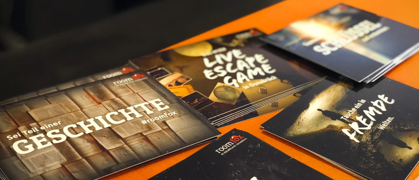Werbekarten von raumbezogenen Abenteuerspielen auf einem orangefarbenen Tisch arrangiert.