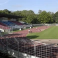 Stadion.tif Sportstadion mit Tartanbahn, Tribüne mit Sitzplätzen und angrenzendem grünen Spielfeld, umgeben von Bäumen.