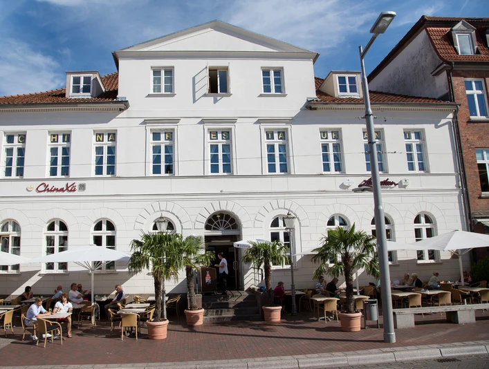 Lavastein_UR3A9092-4_Jens_Butz.jpg Außenbereich mit Sitzplätzen, Gästen und Palmen am Eingang