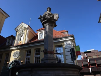Steinerner Brunnen mit Statue eines sitzenden Mannes in historischem Innenhof vor blauem Himmel.