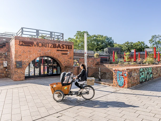 Moritzbastei - Gastronomie à Leipzig Photo de l'entrée supérieure du Moritzbastei sur la place Kurt-Masur à Leipzig, qui abrite un café et un restaurant et où ont lieu de nombreux événements, une cycliste traverse l'image