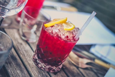 Ein erfrischender, roter Cocktail mit Zitronenscheiben und einem Trinkhalm auf einem Holztisch.