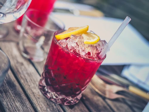 Ein erfrischender, roter Cocktail mit Zitronenscheiben und einem Trinkhalm auf einem Holztisch.