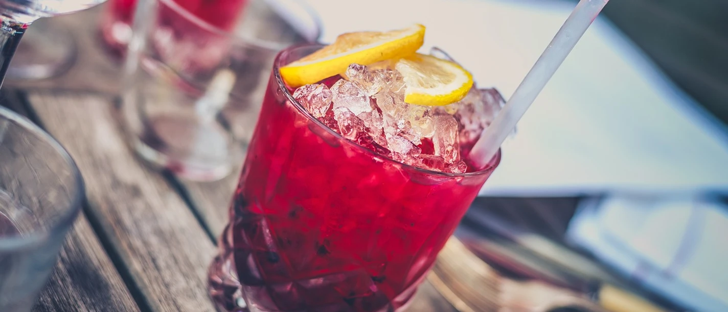 Ein erfrischender, roter Cocktail mit Zitronenscheiben und einem Trinkhalm auf einem Holztisch.