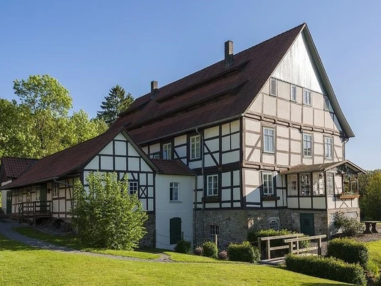 Papiermühle aus Fachwerk mit rotem Dach und Grünflächen, umgeben von Bäumen an sonnigem Tag.