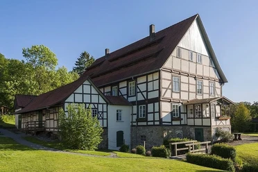 Papiermühle Plöger.jpg Papiermühle aus Fachwerk mit rotem Dach und Grünflächen, umgeben von Bäumen an sonnigem Tag.